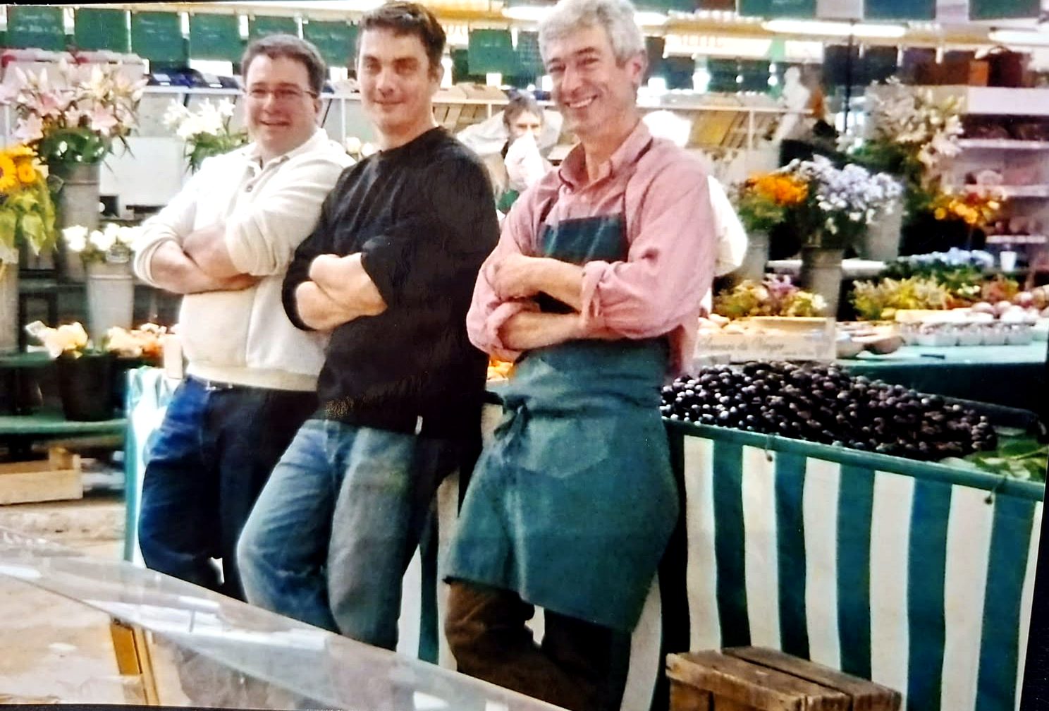 Matthieu, Antoine et Olivier Daire, bras croisés et souriants, devant l’étal de fleurs et d’olives